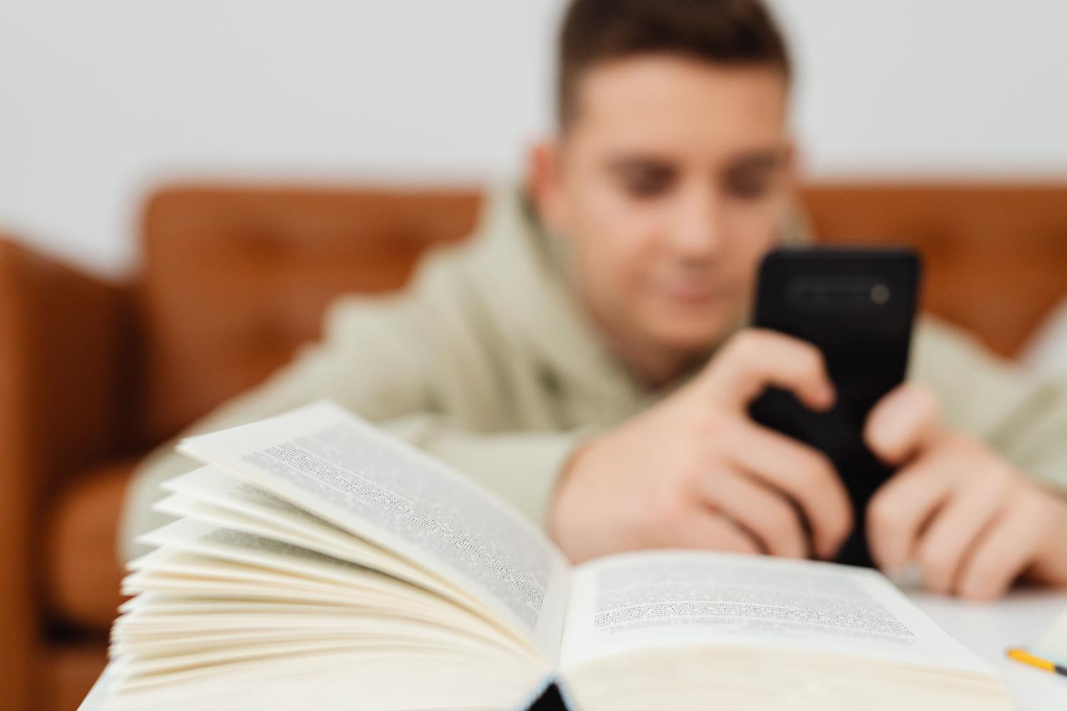Estudiante utilizando su móvil junto a un libro abierto para resolver dudas académicas