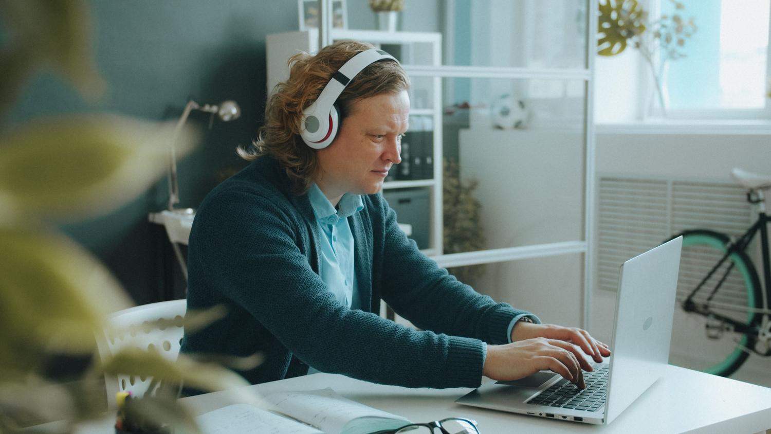 Hombre con auriculares blancos trabajando en un portátil, ilustrando el uso de música para concentrarse.