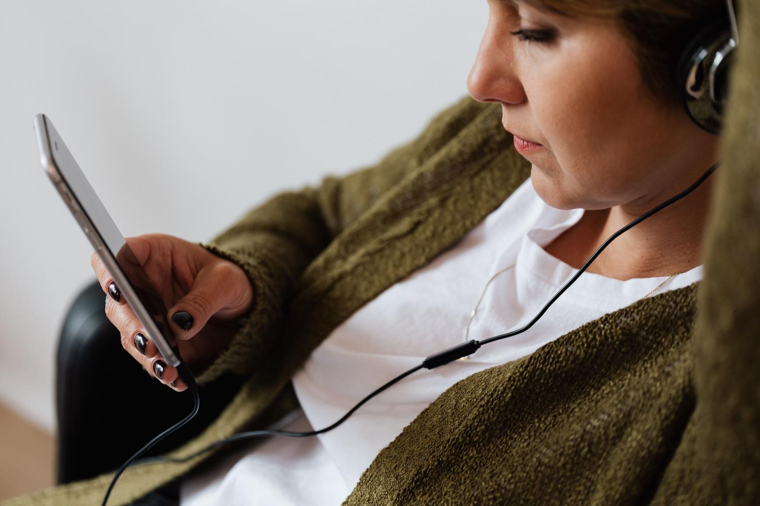 Mujer utilizando un smartphone con auriculares, representando el consumo de datos móviles al hacer streaming de música.