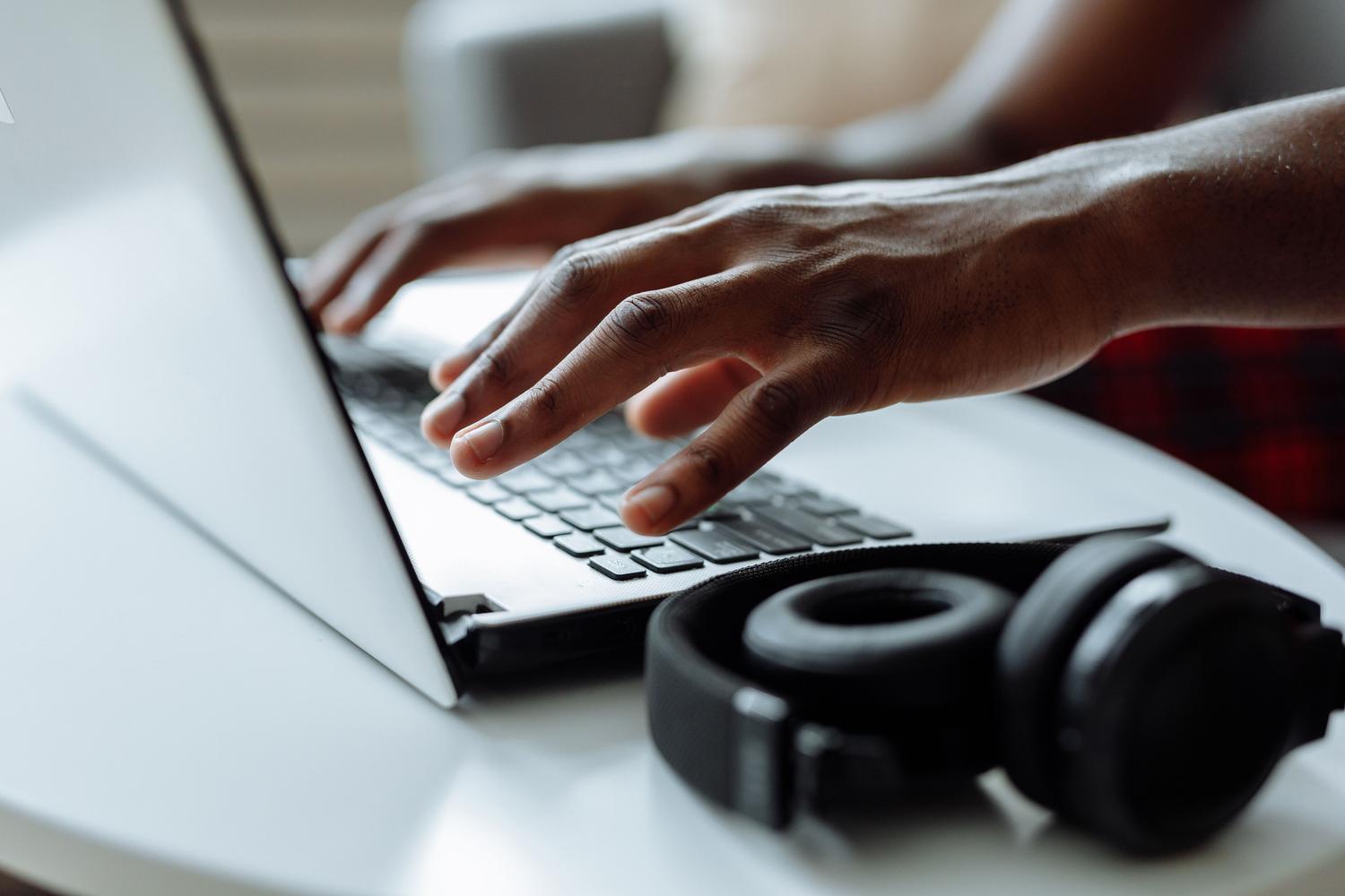 Primer plano de manos escribiendo en un portátil con auriculares al lado, representando la productividad.
