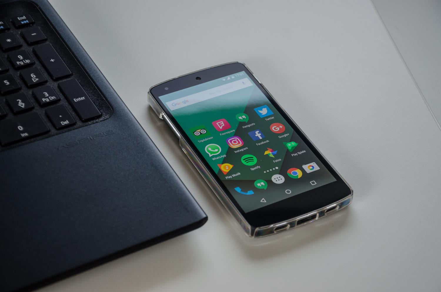 Primer plano de un smartphone Android junto al teclado de un ordenador portátil, destacando la interacción entre el móvil y el PC.