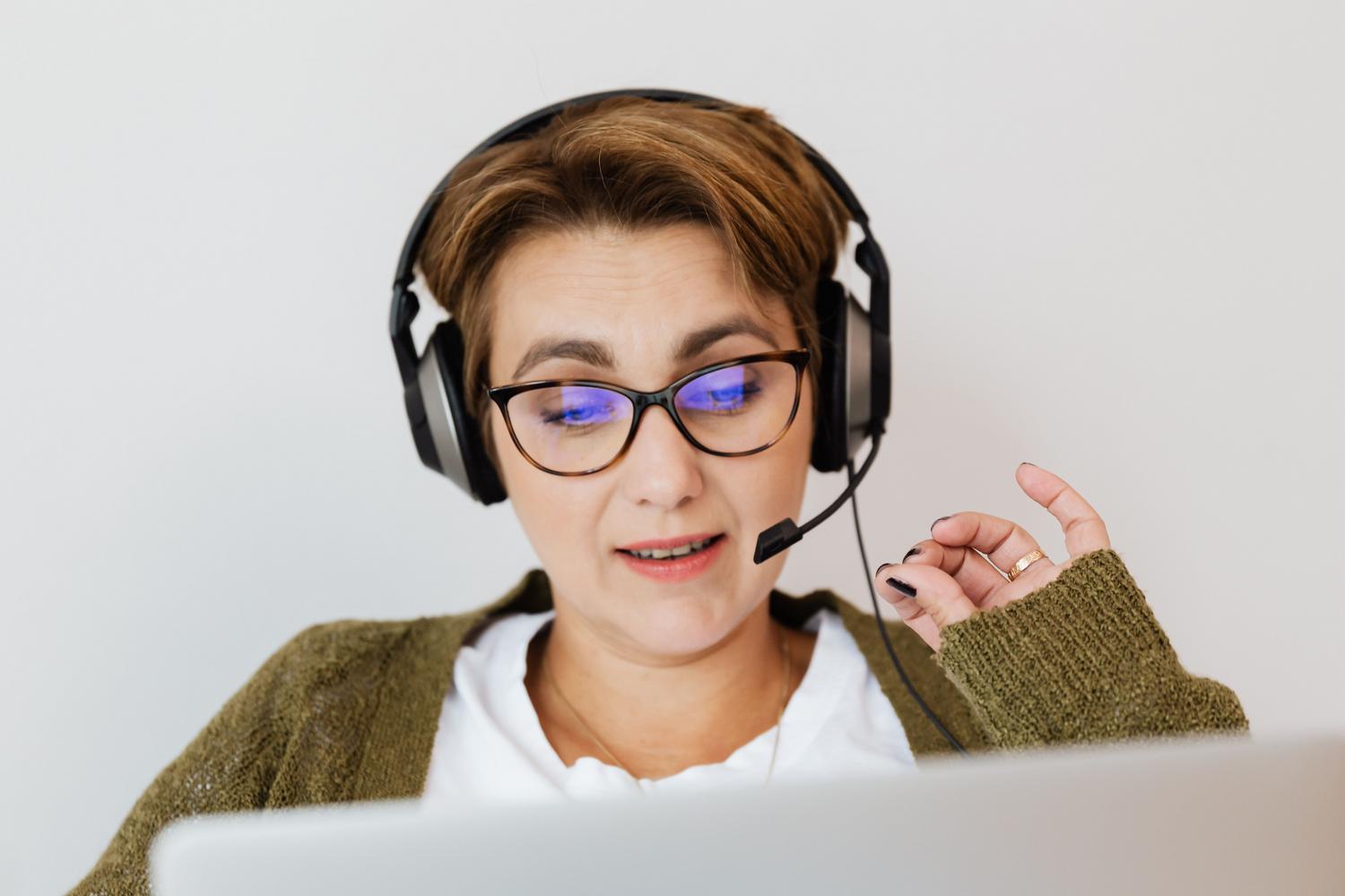 Mujer profesional con auriculares y micrófono dictando texto a su ordenador portátil en un ambiente de trabajo moderno.