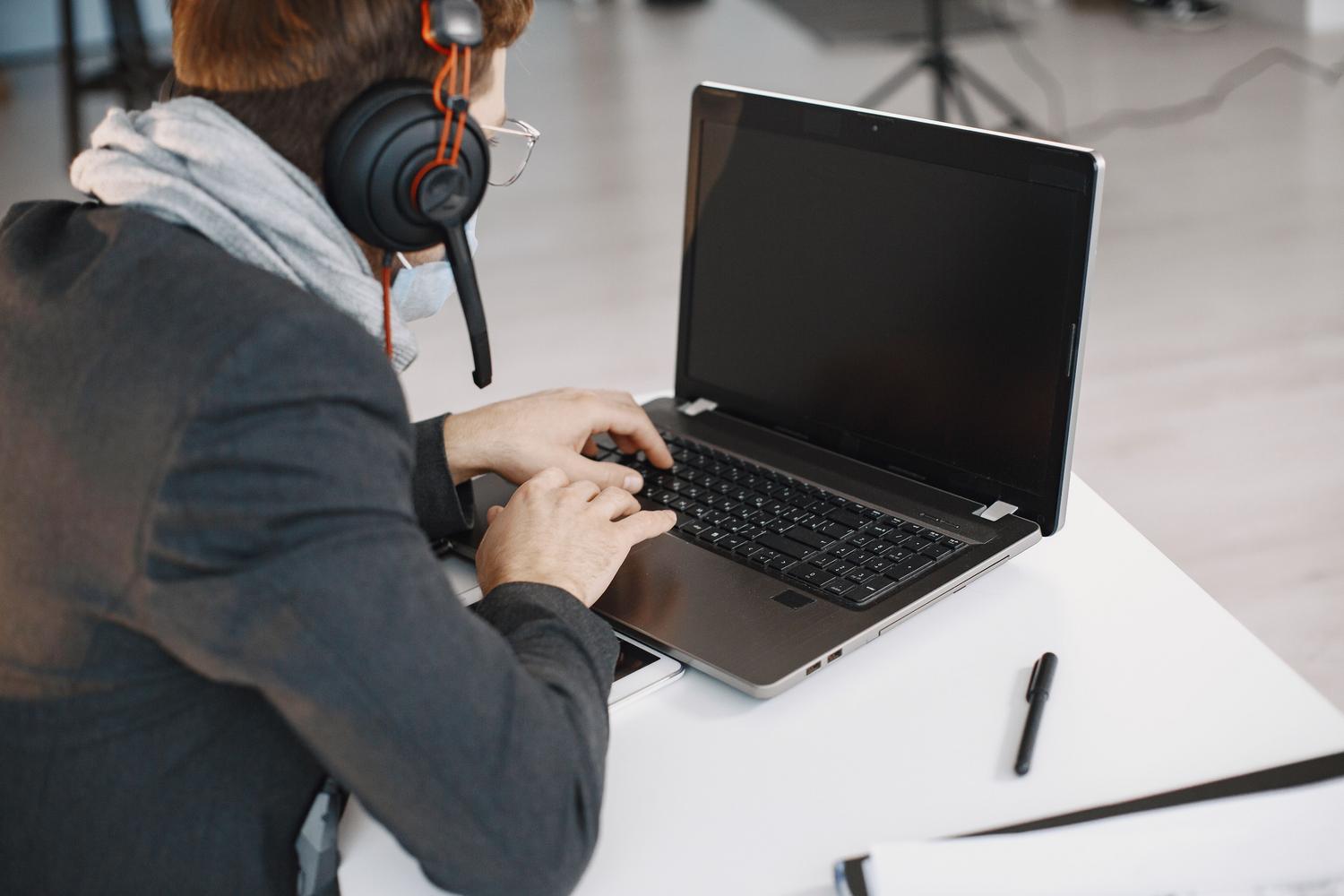 Hombre en una oficina moderna usando un ordenador portátil y auriculares, enfocado en la productividad mediante entrada de voz.