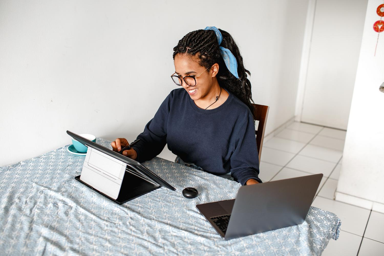 Mujer trabajando en multitarea utilizando simultáneamente un portátil y una tablet, reflejando un flujo de trabajo híbrido y versátil.