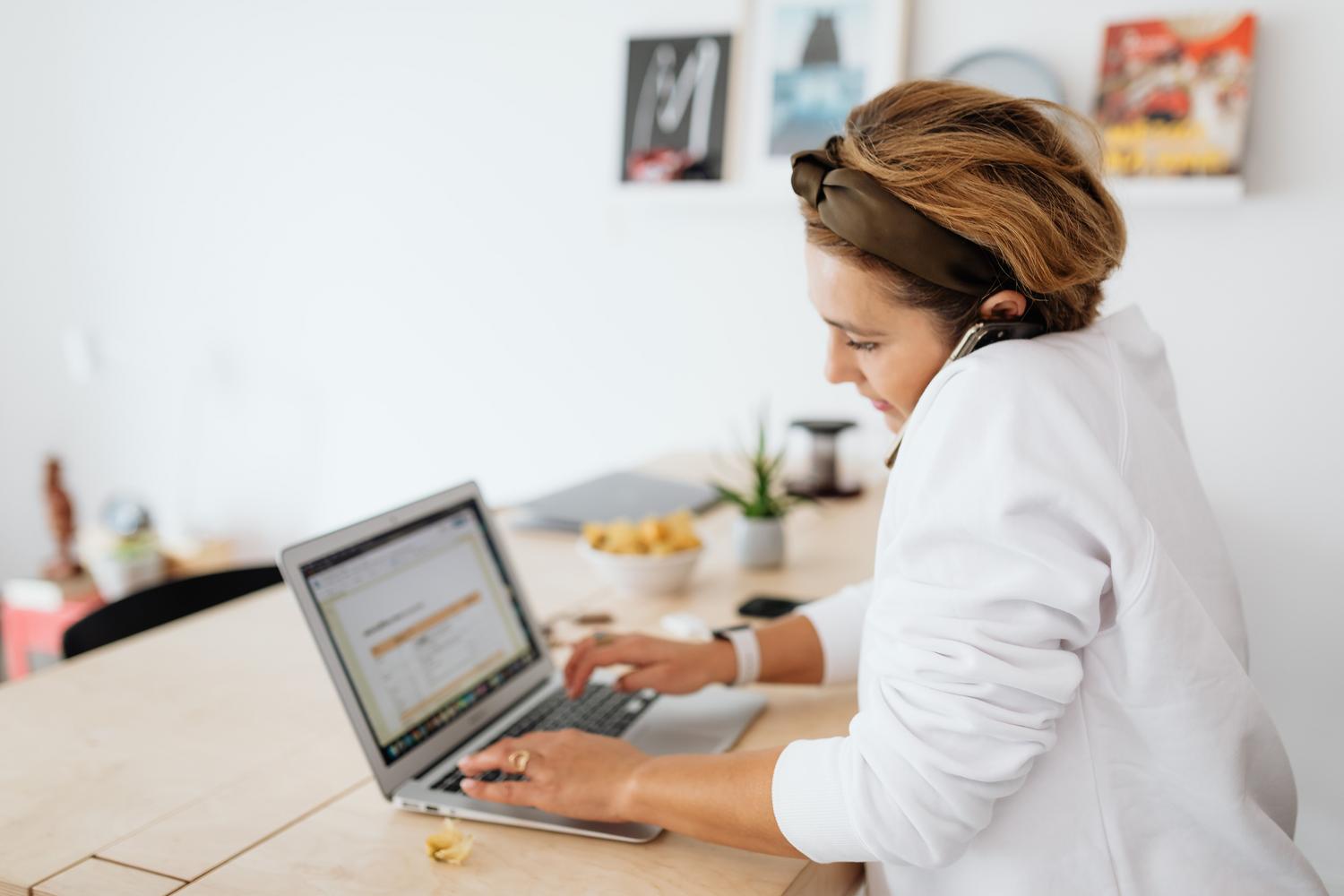 Mujer multitarea utilizando un portátil y un teléfono inteligente en un entorno moderno.
