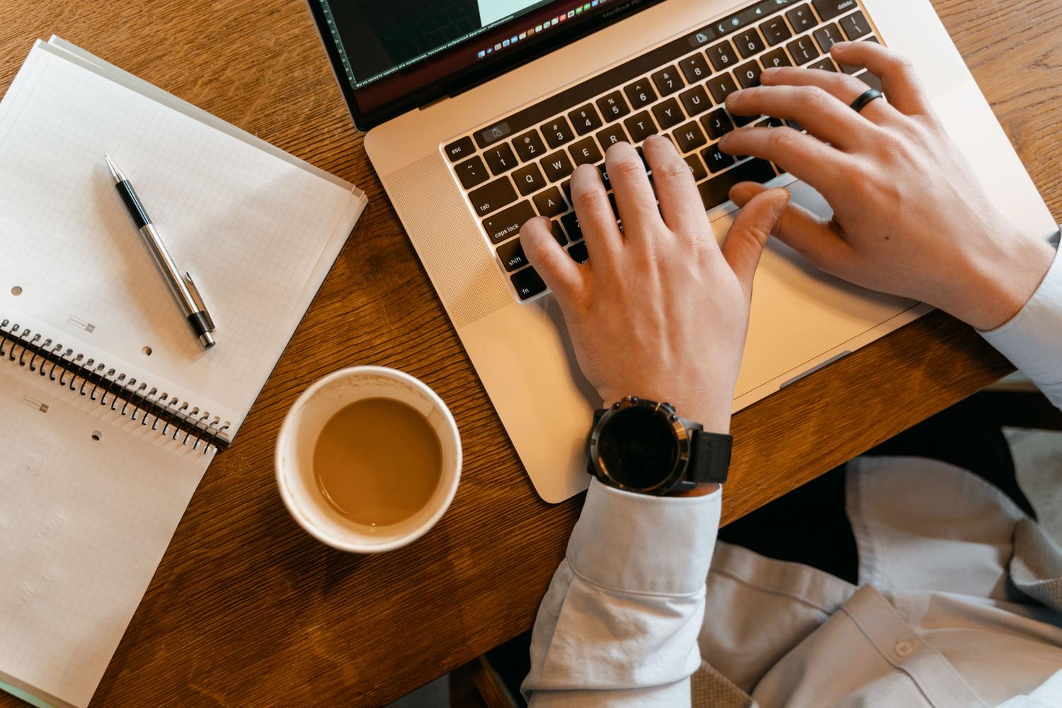 Primer plano de manos escribiendo en un teclado de portátil junto a una taza de café, simbolizando un entorno de navegación productivo.