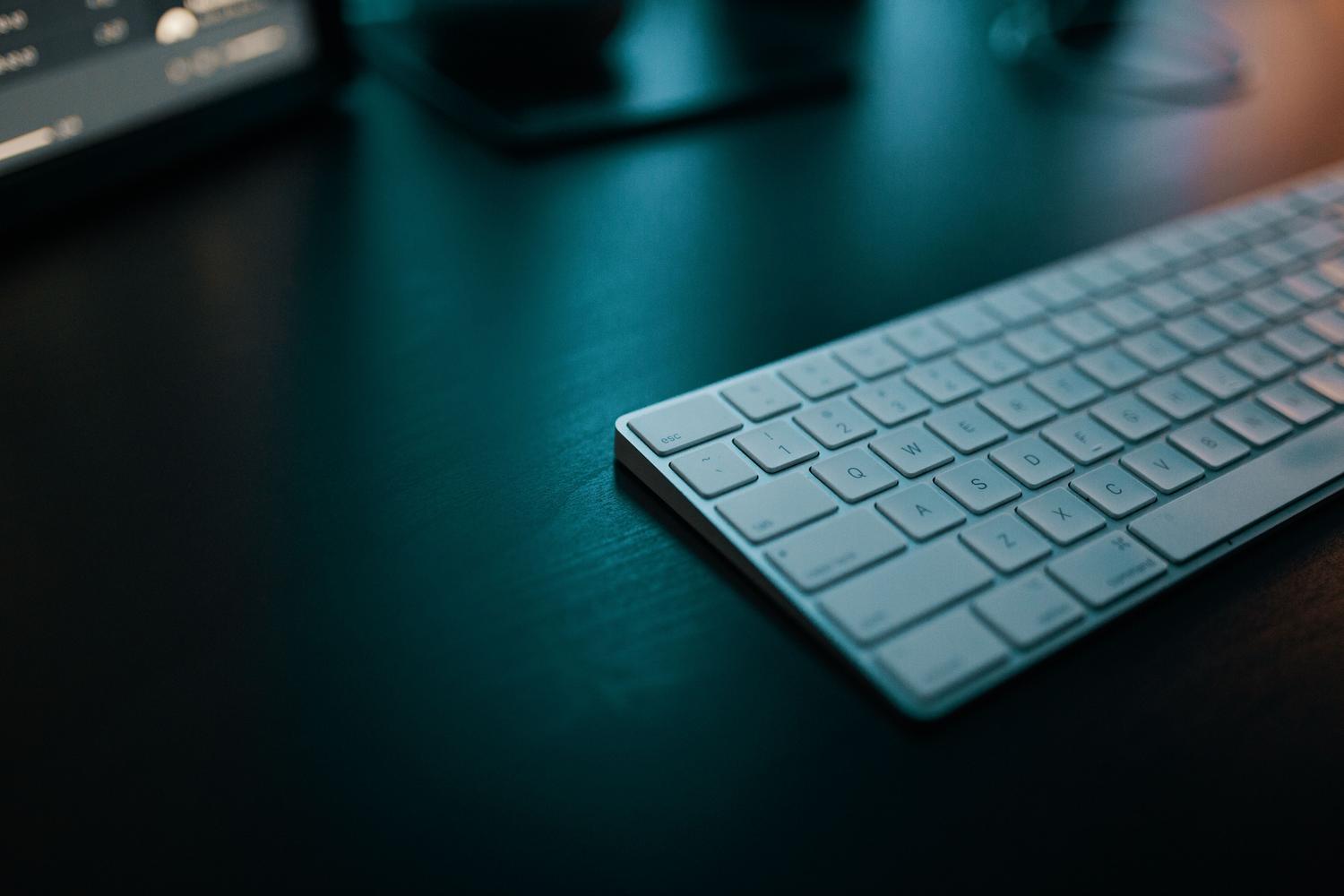 Teclado inalámbrico blanco minimalista sobre un escritorio oscuro con iluminación tecnológica, ideal para contenido de software.