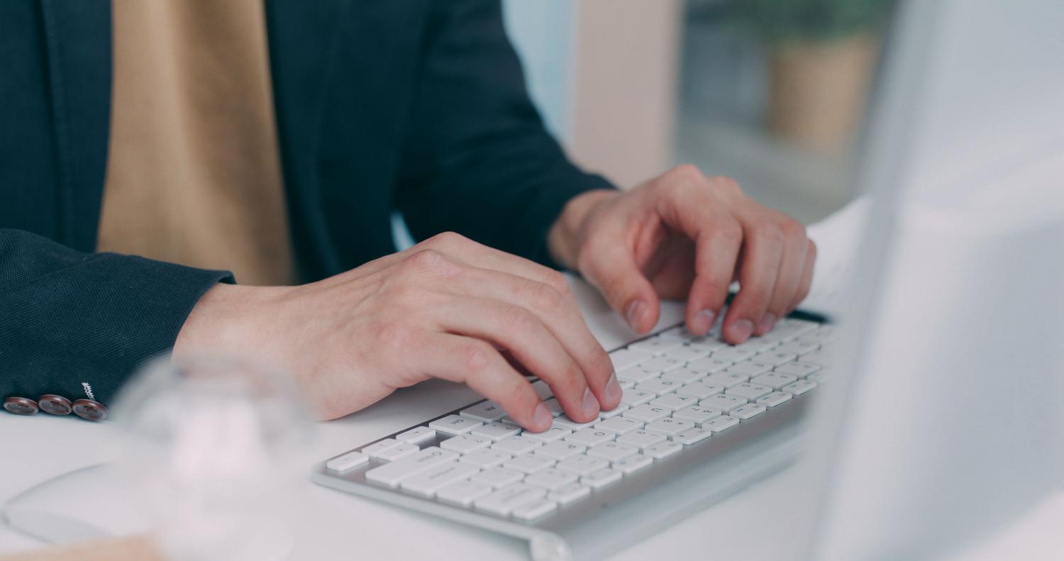 Primer plano de manos de un profesional escribiendo en un teclado blanco en un entorno de oficina moderno.