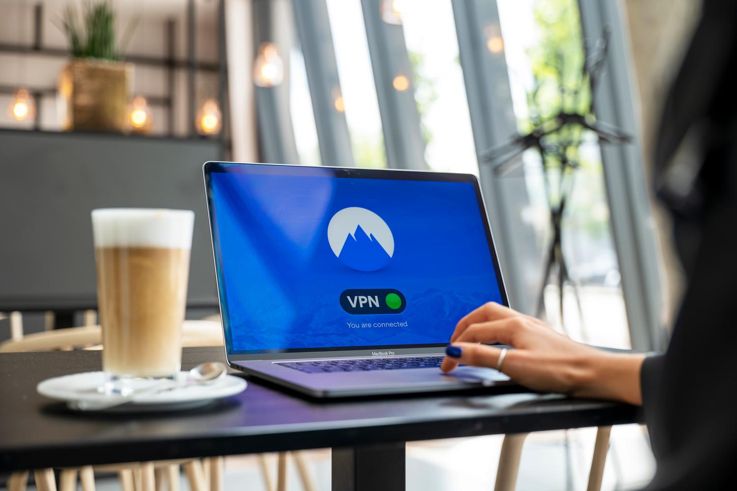 Persona utilizando una conexión VPN en un ordenador portátil en una cafetería, representando la libertad y seguridad del trabajo remoto.