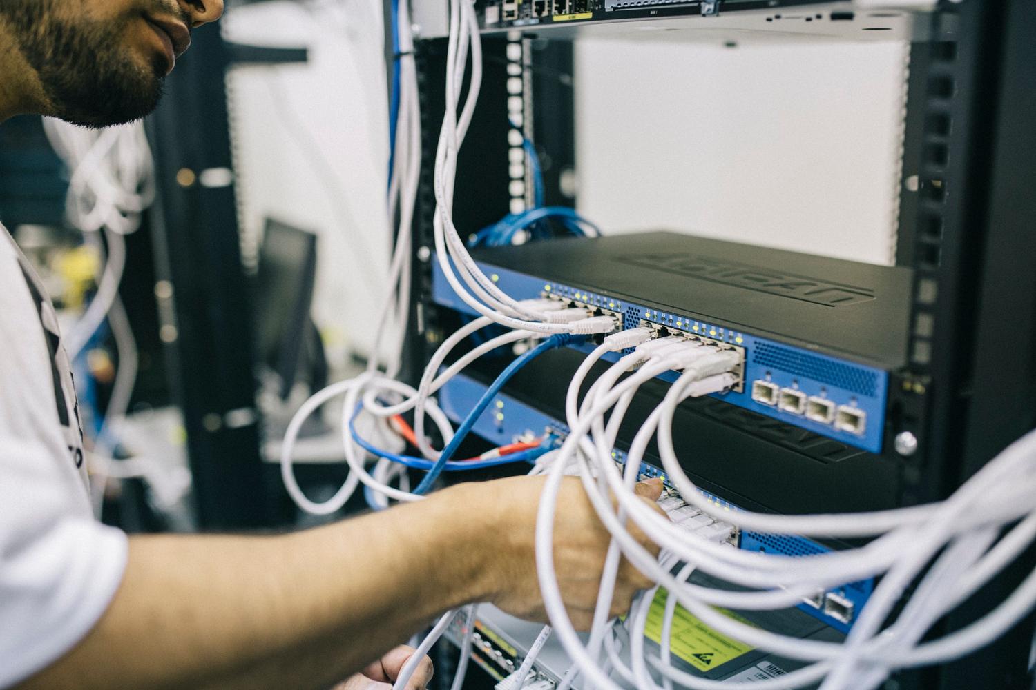 Profesional de IT organizando y asegurando el cableado de red en un rack de servidores para optimizar la seguridad física.