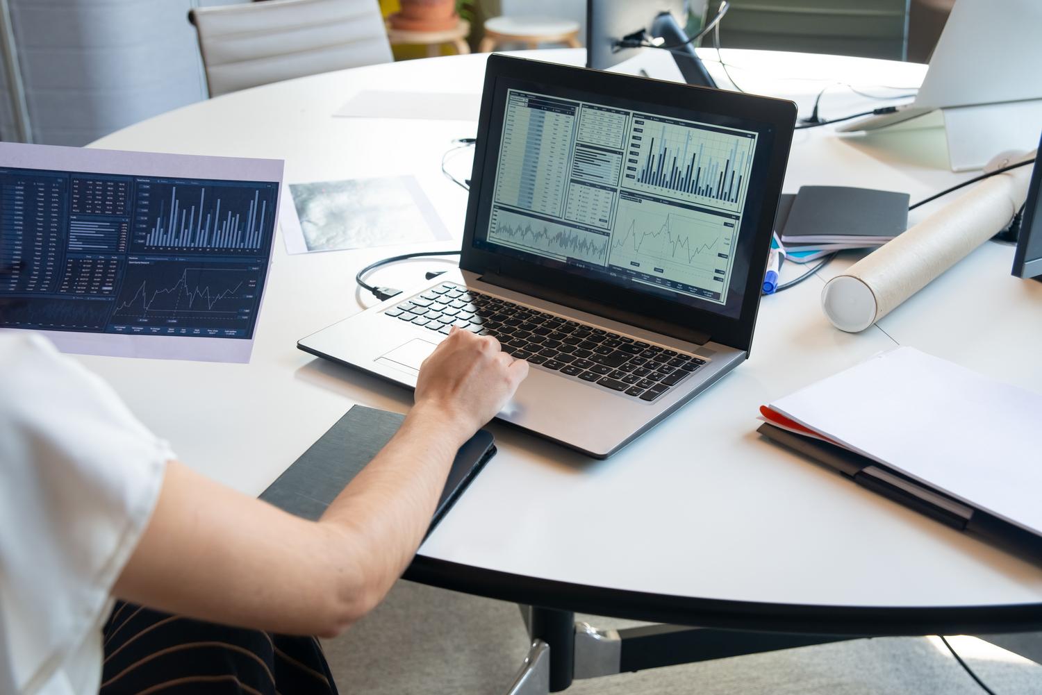 Profesional analizando tablas de datos y gráficos financieros en un portátil en una oficina luminosa y minimalista.