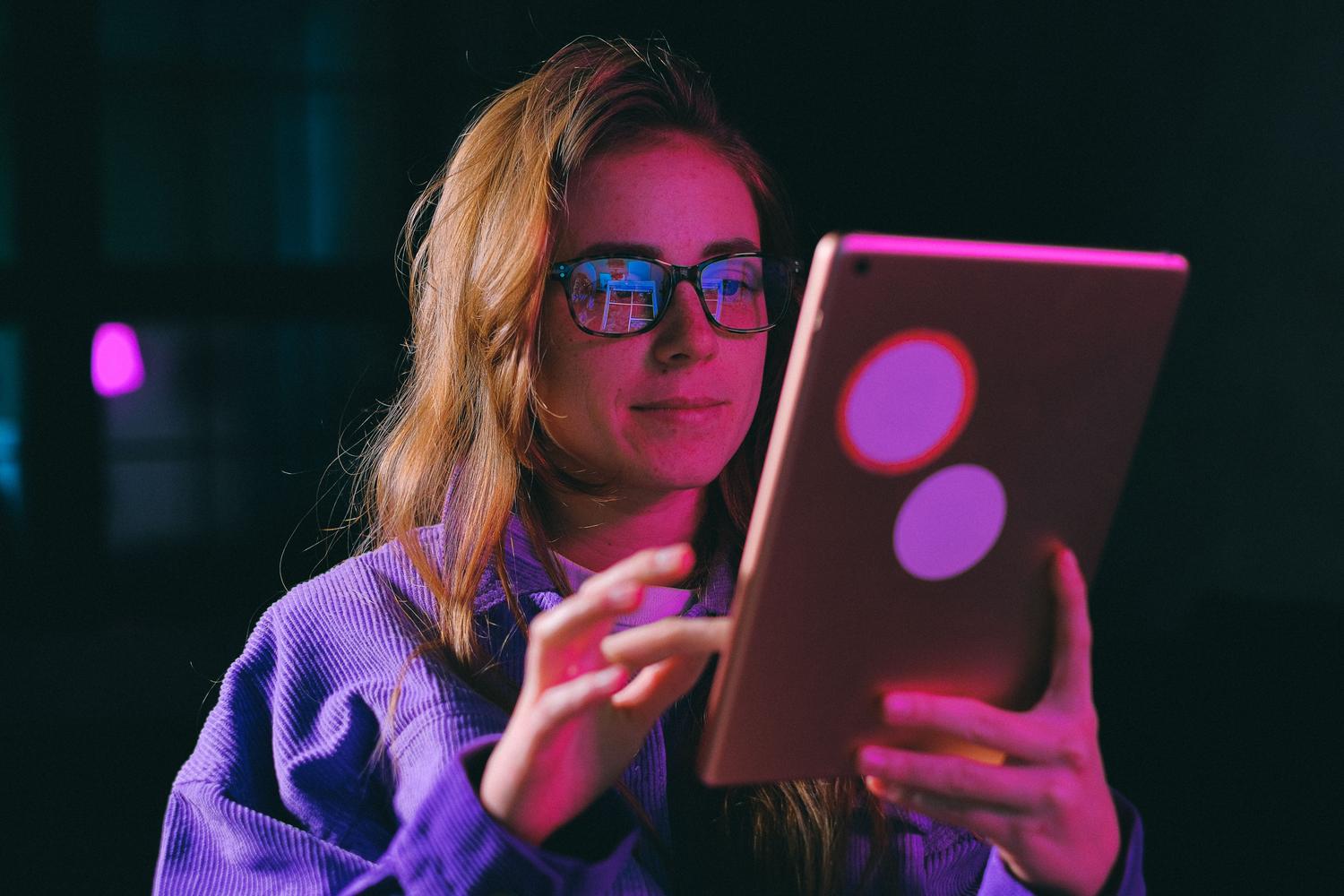 Mujer concentrada usando una tablet en una habitación oscura, representando la realización de investigaciones sensibles con privacidad.