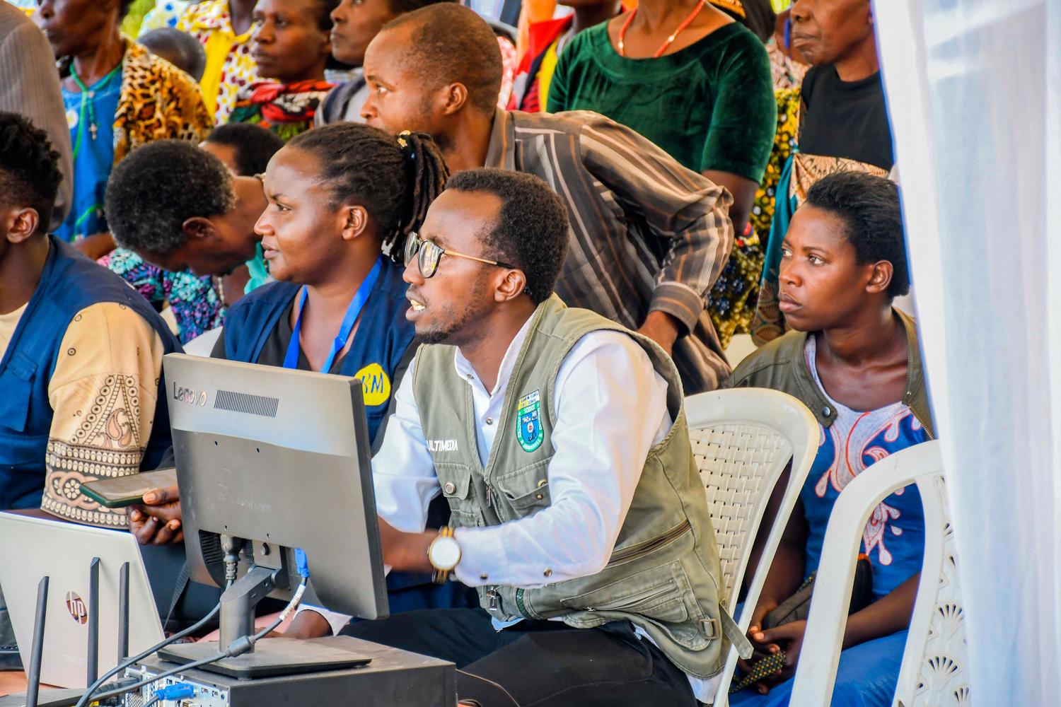 A diverse group of adults in Rwanda interacting with technology at a community event, illustrating the arrival of AI in unexpected places. A diverse group of adults in Rwanda interacting with technology at a community event, illustrating the arrival of AI in unexpected places.