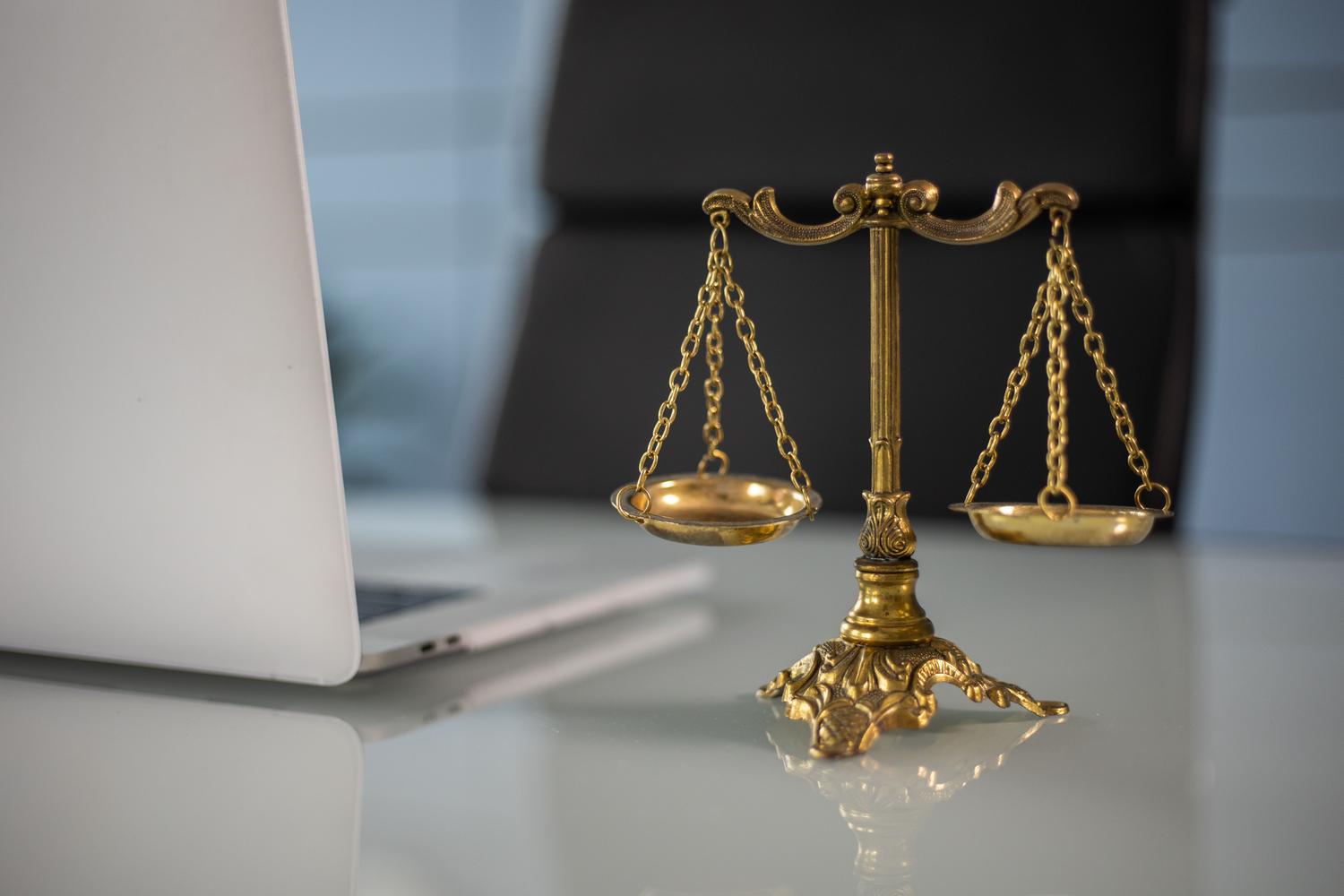 Balanza de la justicia junto a un ordenador portátil, representando la fusión de los requisitos legales y la tecnología de transcripción digital.