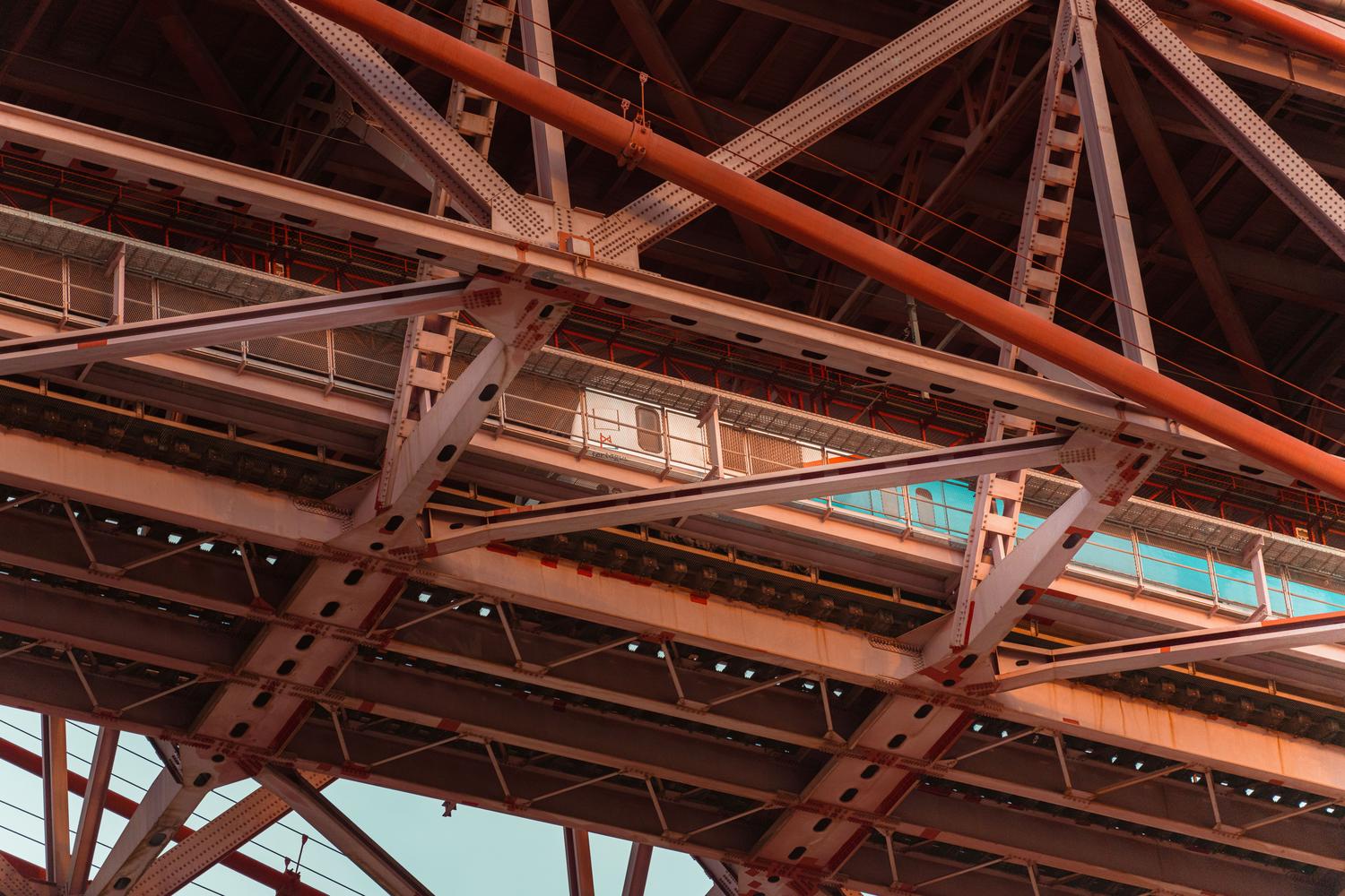 Detalle arquitectónico de las vigas y estructuras de acero de un puente moderno, representando las infraestructuras pesadas sujetas a monitoreo.