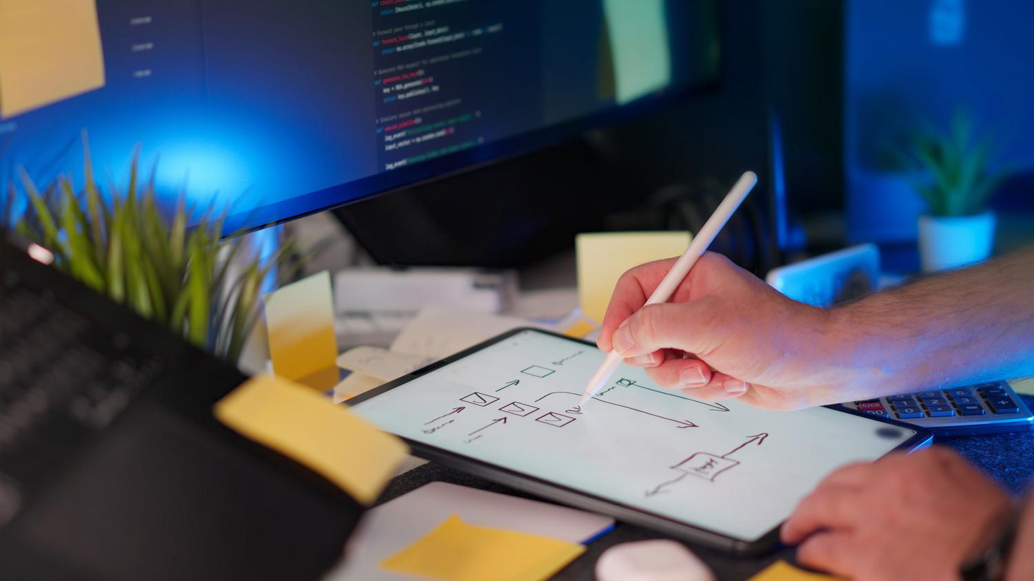 Espacio de trabajo moderno con bocetado digital y código Espacio de trabajo moderno con bocetado digital en tablet y código en monitor, representando el diseño de flujos de usuario.