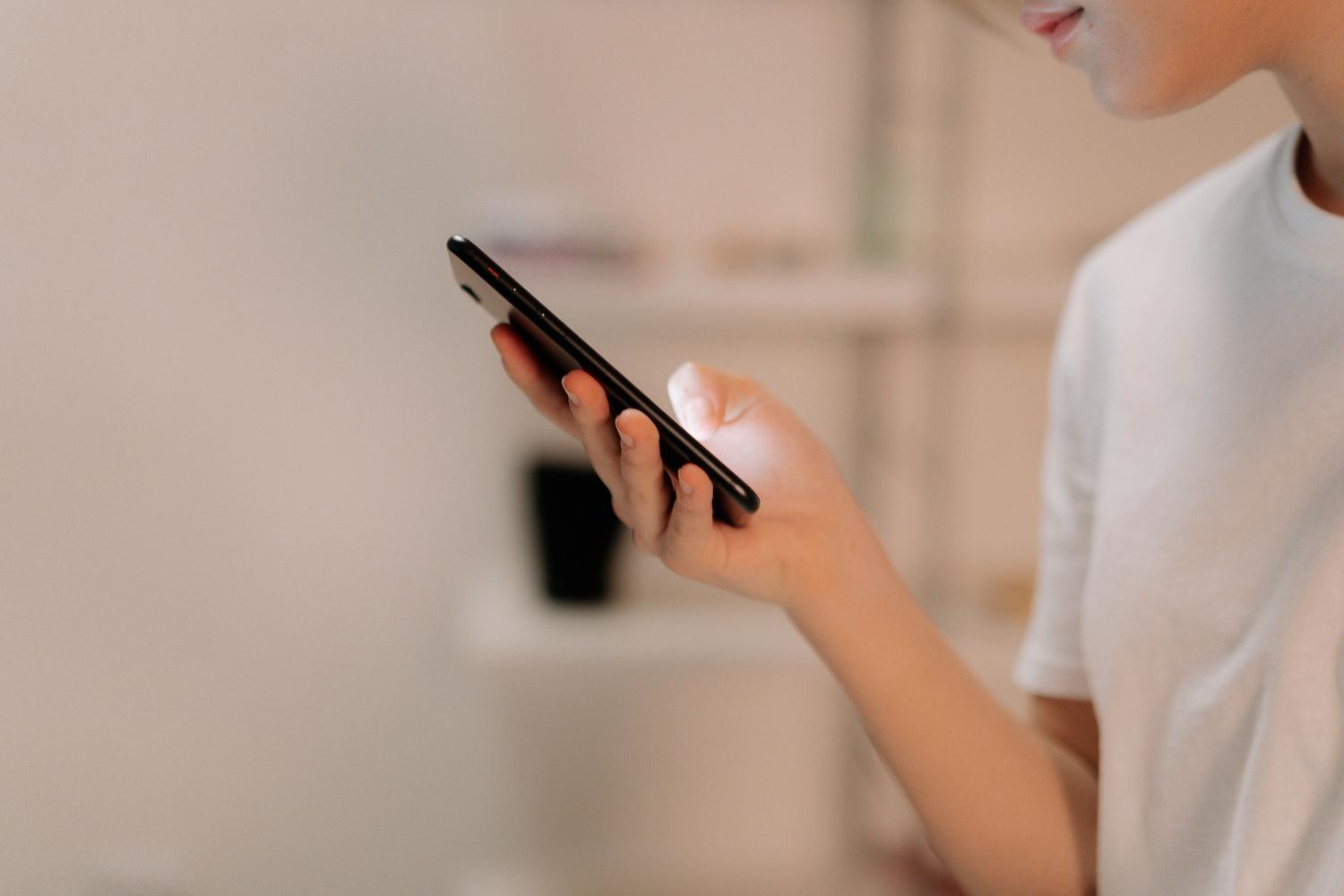 Osoba korzystająca z ekranu nowoczesnego smartfona w pomieszczeniu zamkniętym, ilustrująca nawigację po menu Ustawień.