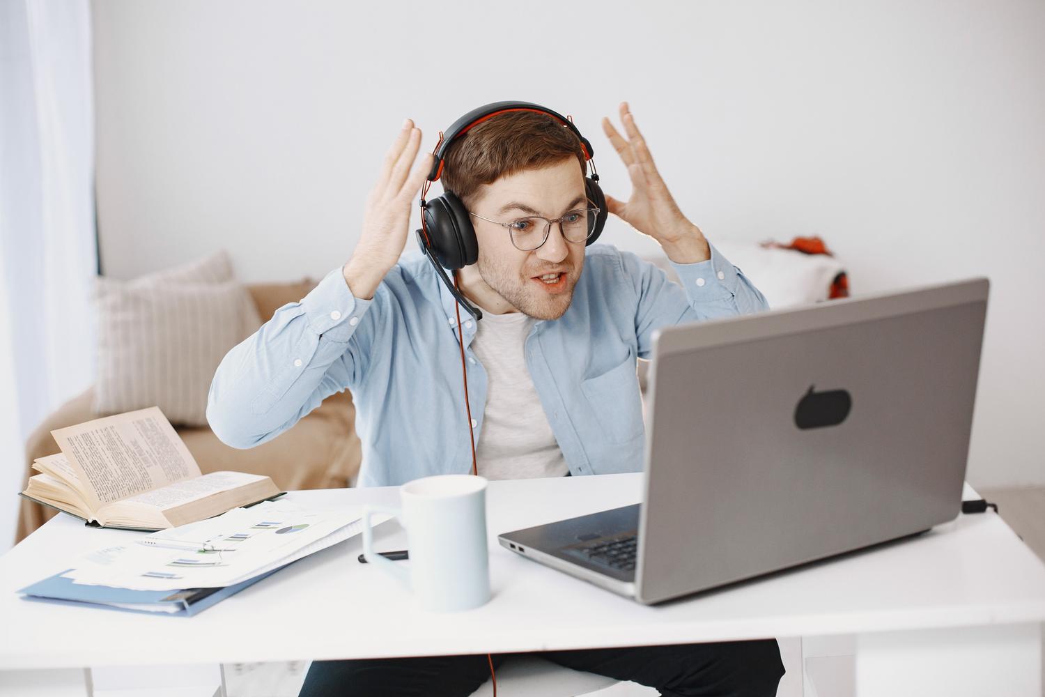 Vīrietis, kas strādā attālināti un pauž neapmierinātību pie datora, ideāli piemērots videozvanu un VoIP pārtraukumu attēlošanai.