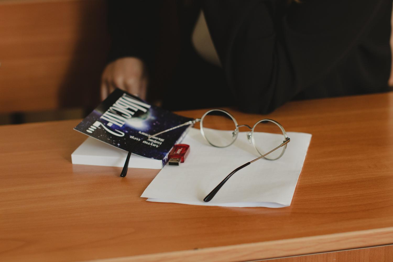 Unitate flash USB pe un birou cu cărți și ochelari, simbolizând o capsulă digitală a timpului sau materiale de studiu.