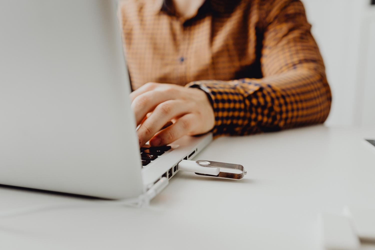 Persoană care folosește un laptop cu o unitate USB conectată pentru a rula software portabil.
