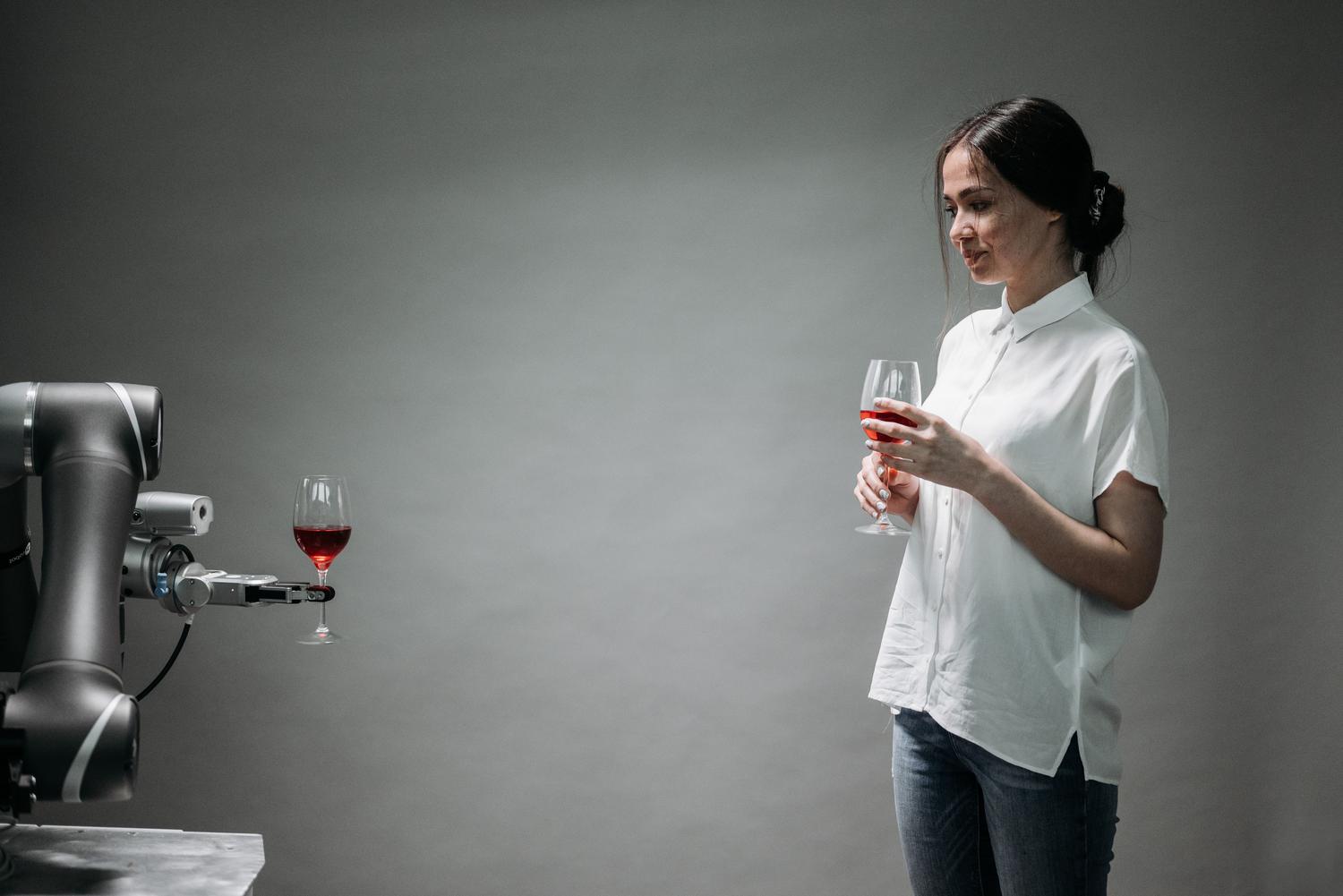 Robot camarero sirviendo una copa de vino a una clienta en un entorno moderno, ejemplificando la robótica de servicio en la hostelería.