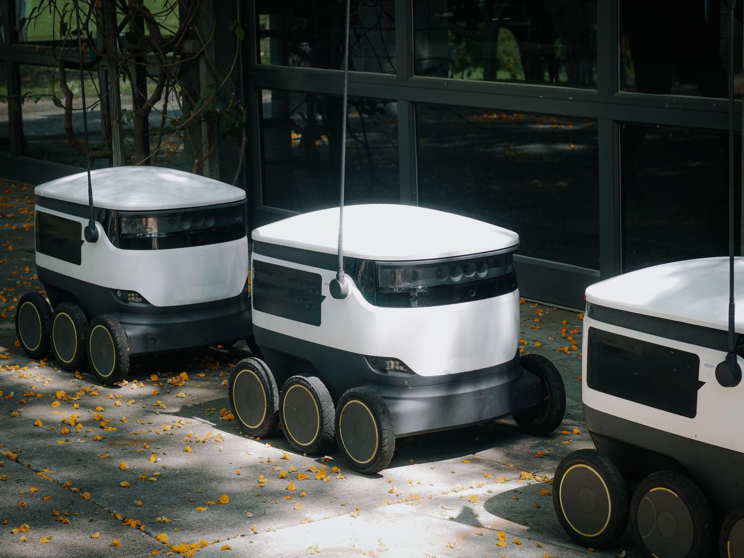 Robots de entrega autónomos navegando por una acera urbana durante el día, mostrando la logística profesional automatizada.