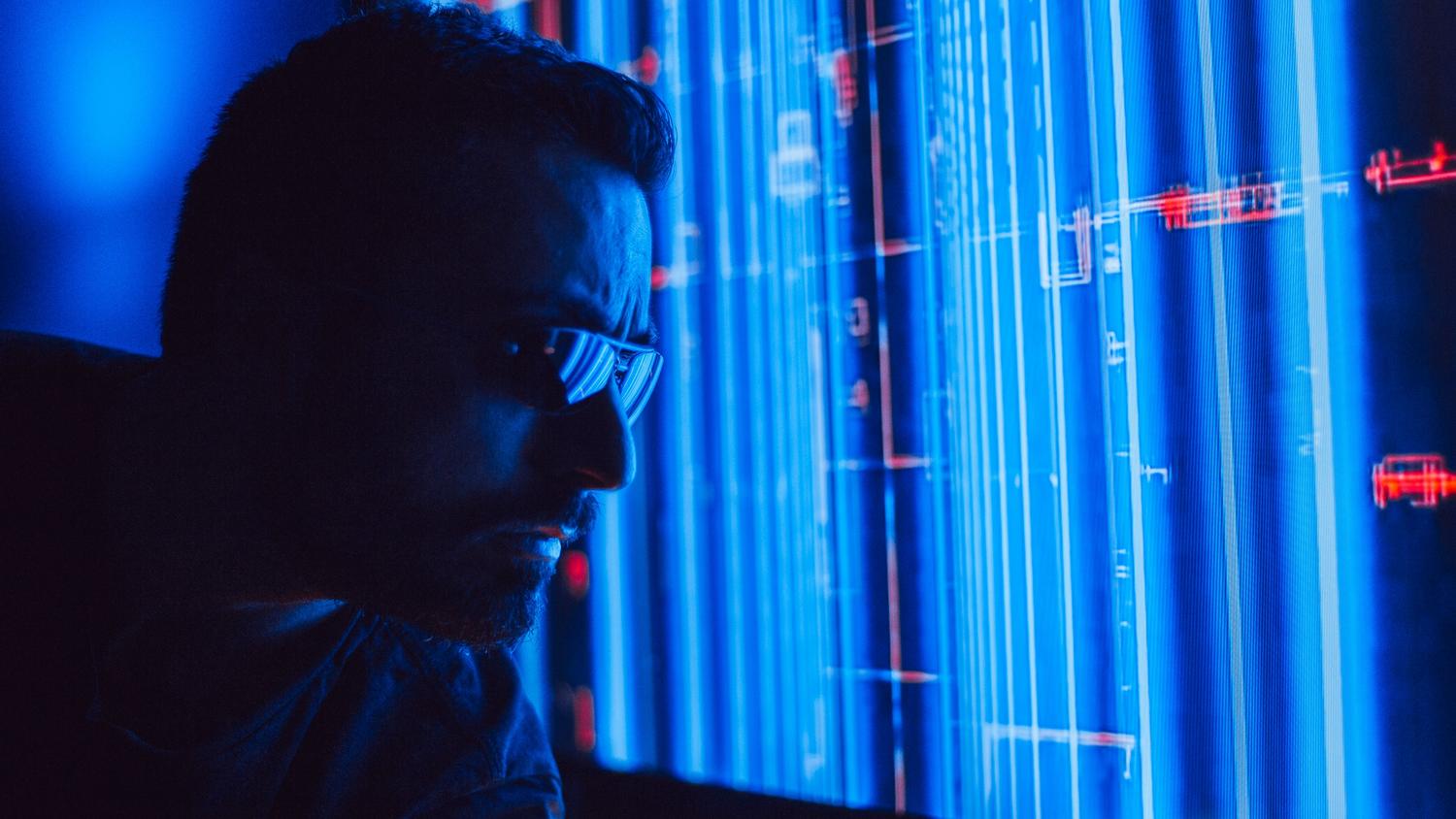 Profesional analizando una pantalla holográfica azul, simbolizando el uso de inteligencia artificial y monitorización avanzada de amenazas.